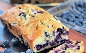 blueberry cream cheese bread sliced on a wooden board with fresh blueberries