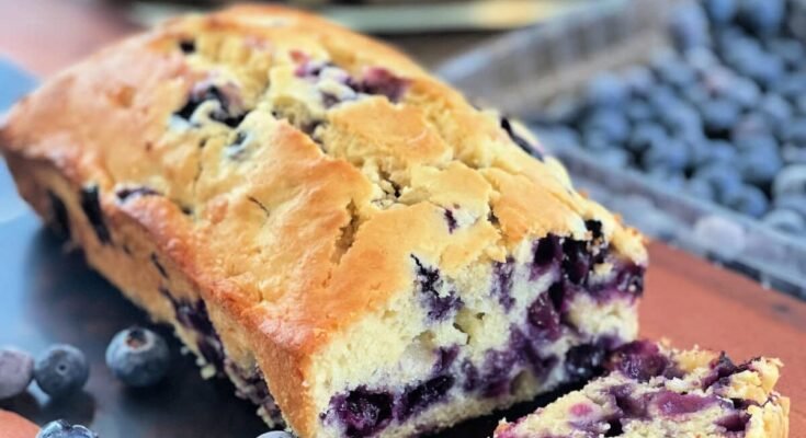 blueberry cream cheese bread sliced on a wooden board with fresh blueberries